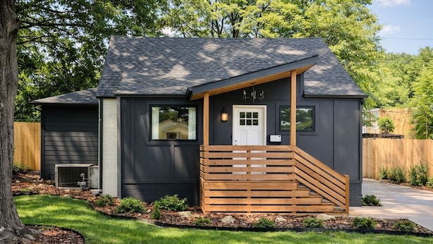 Une maison moderne à l’extérieur sombre, avec un escalier en bois menant à la porte d’entrée et une pelouse bien entretenue.