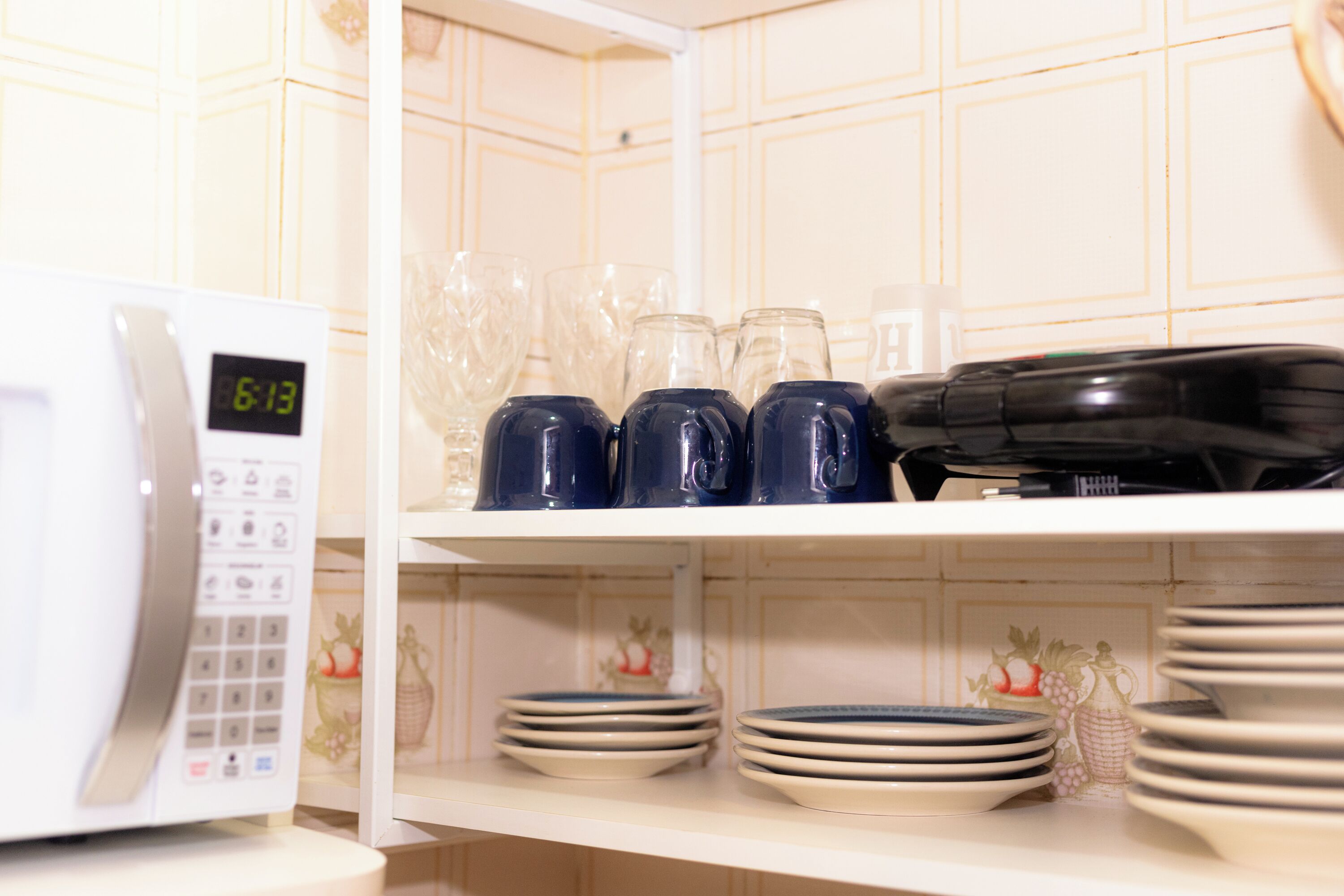 A kitchen with a microwave on the left, shelves with plates, bowls, and blue mugs.