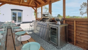 Ein Outdoor-Kochbereich mit Grill, Backofen und Essplatz, gedeckt mit Tellern und Gläsern.