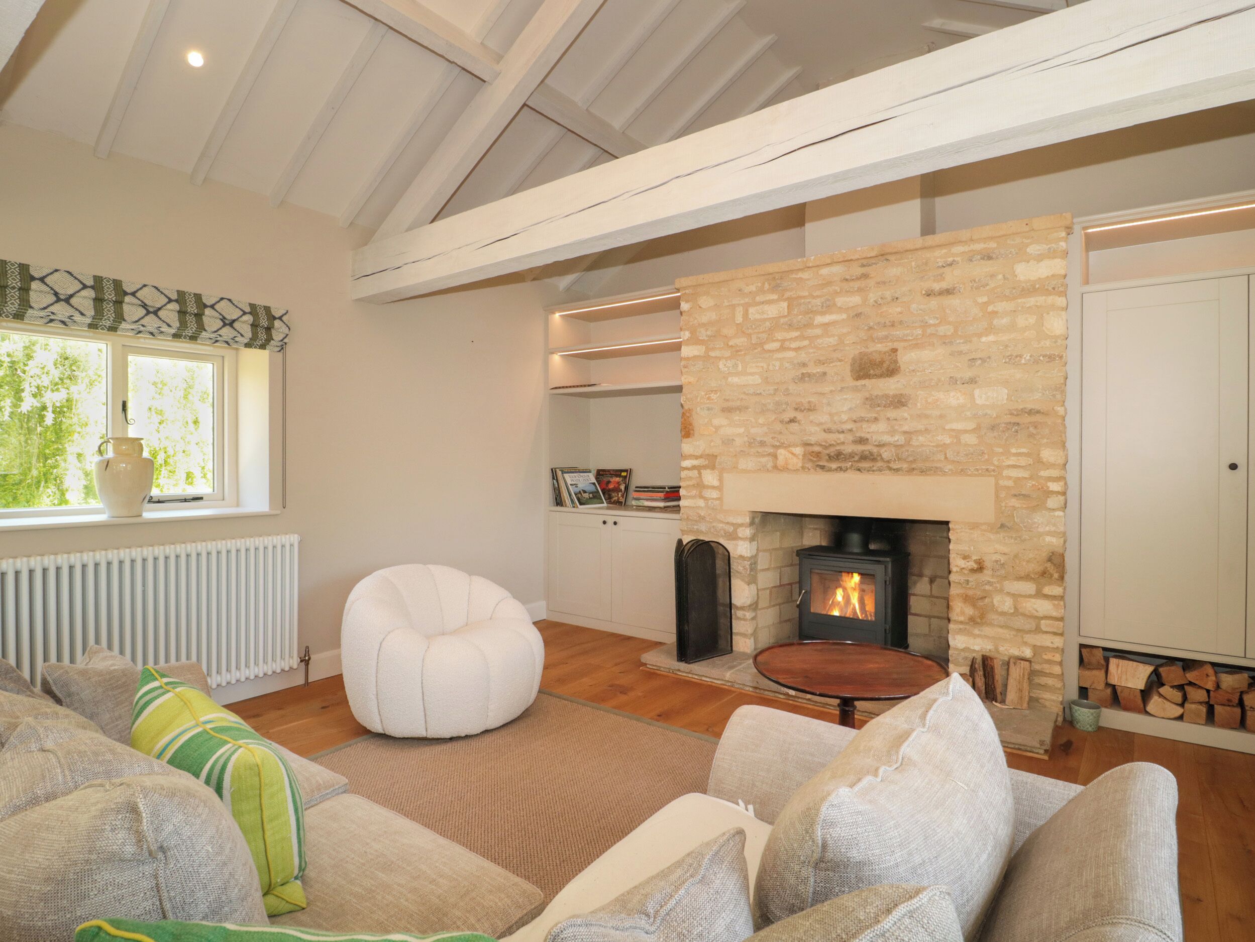 A cozy living room with a stone fireplace, a comfortable sofa, and a window with a view of greenery.