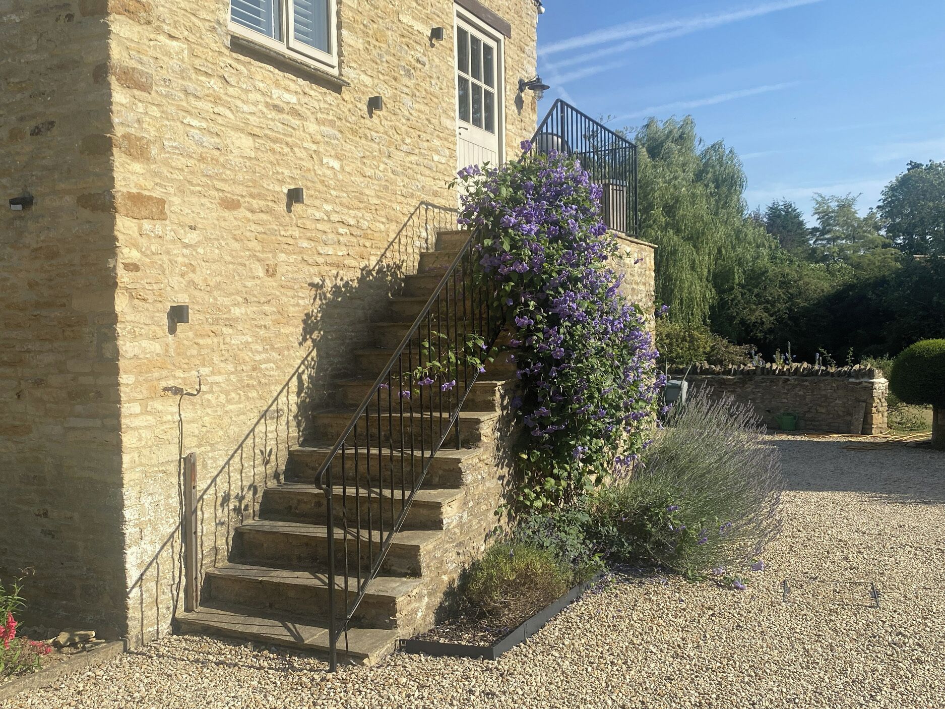 Un bâtiment en pierre avec un escalier menant à un balcon, entouré de gravier et de verdure.