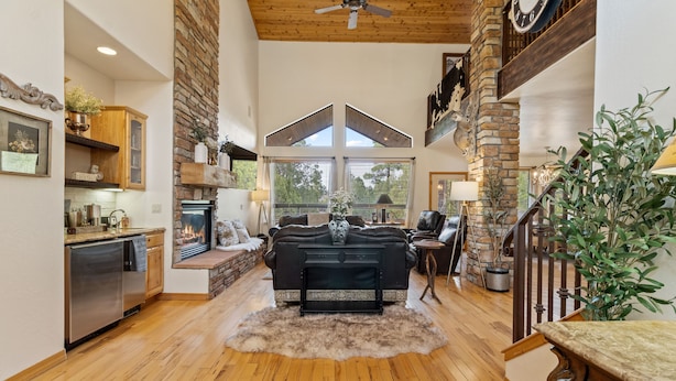 A spacious living area with a fireplace, wooden floors, and a high ceiling with a fan. - European Rustic Mountain Retreat in Torreon (Show Low)
