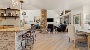 A spacious living area with a stone pillar, a kitchen with a brick backsplash, and a dining area with a large table and chairs. - European Rustic Mountain Retreat in Torreon (Show Low)