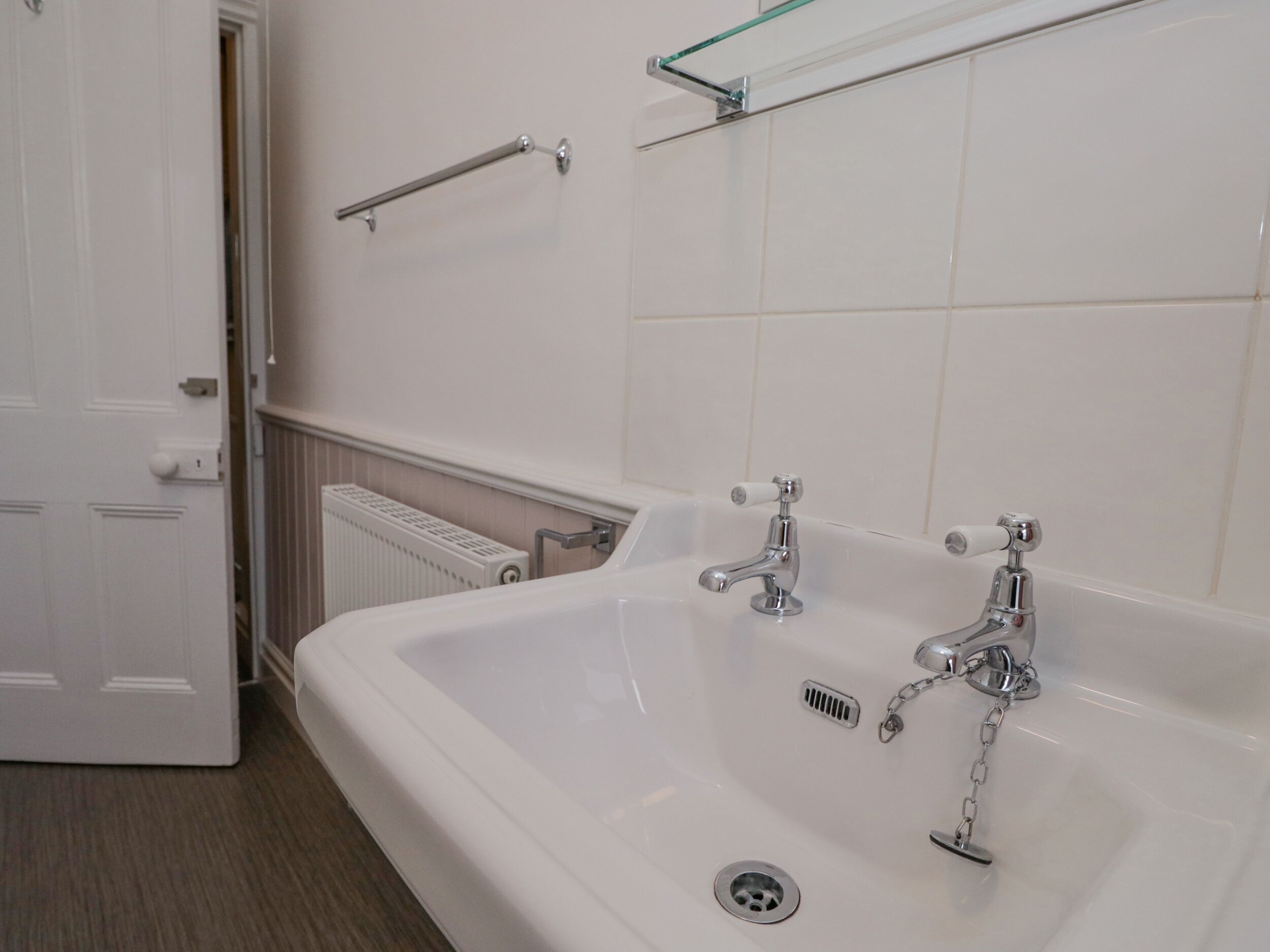 A bathroom with a white sink, two faucets, a towel rack, and a radiator.