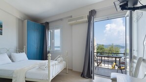 Quarto com cama, guarda-roupa azul, varanda com mesa e cadeiras, e vista para o exterior.