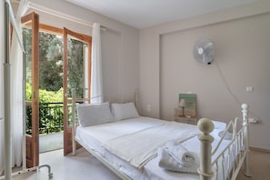A bedroom with a bed, a fan, a window, and a view of greenery.
