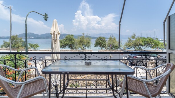 Uma varanda com mesa e cadeiras, vista para o mar e montanhas ao longe.