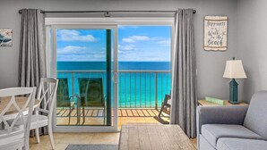Une chambre avec un balcon donnant sur une plage, un coin repas avec des chaises, un canapé et une lampe.