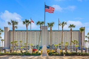 A hotel with a central flagpole, palm trees, and a parking lot.