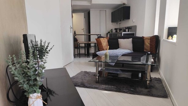 A modern living room with a glass coffee table, black sofa, and a dining area in the background.