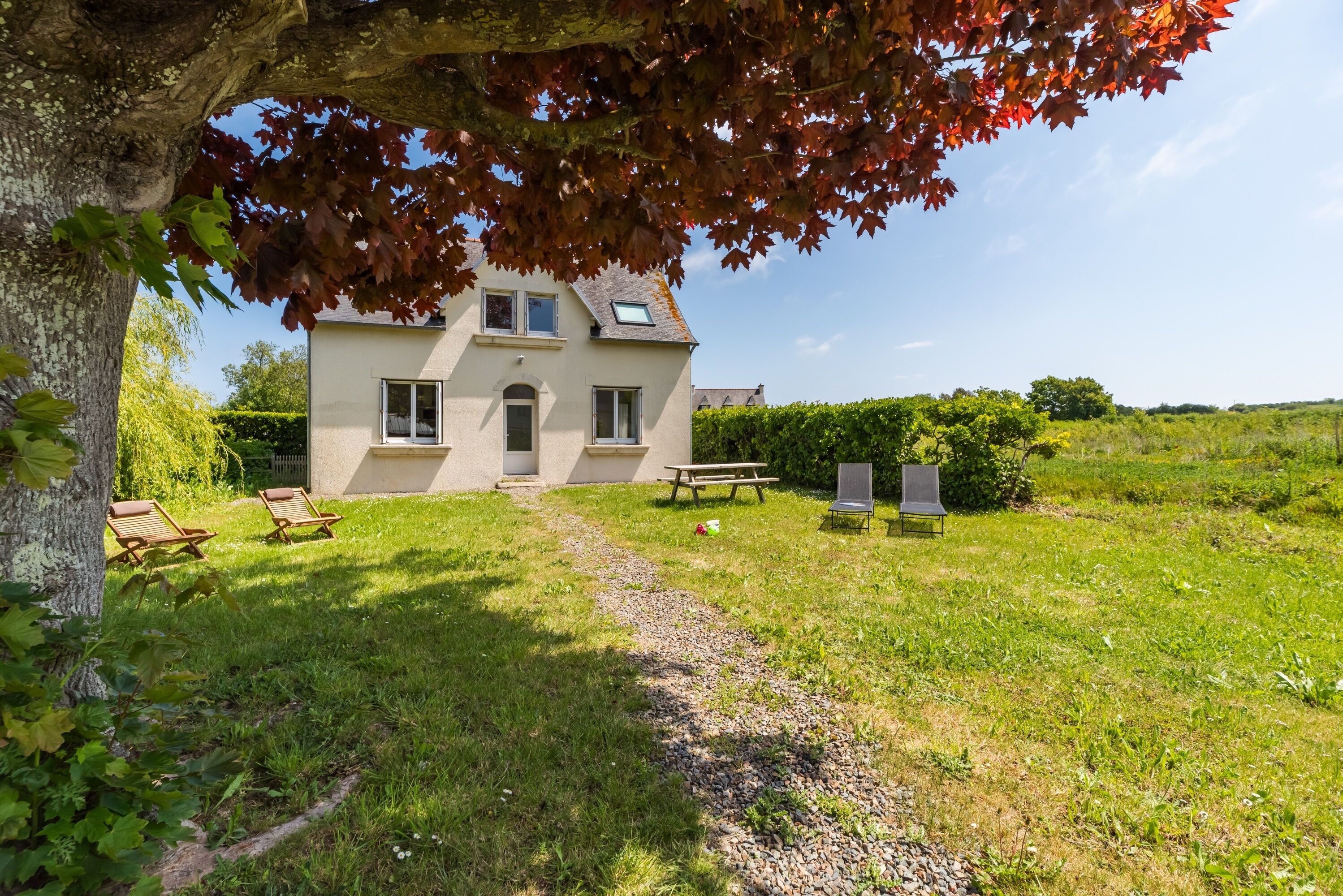 Une maison avec un chemin pavé menant à une porte, entourée d’une pelouse verdoyante et d’arbres.