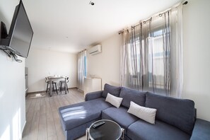 Uma sala de estar moderna com um sofá cinzento, uma mesinha de centro redonda e uma televisão de ecrã plano na parede.