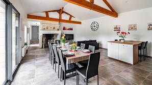 Un vaste espace dédié à la salle à manger, avec une longue table, des chaises noires et un îlot central en bois doté de sièges.