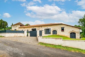 A two-story building with a tiled roof, a gated entrance, and a small garden area.