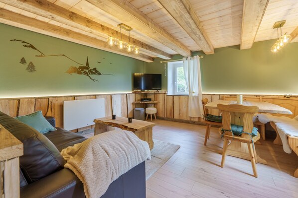 A cozy cabin interior with a wooden ceiling, a television, a dining table, and a sofa.
