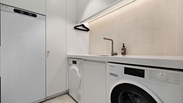 Une buanderie moderne équipée d’un lave-linge à chargement frontal, d’un sèche-linge et d’un évier avec un distributeur de savon.