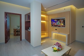 A modern living room with a flat-screen TV mounted on the wall, a dining table with a floral centerpiece, and a wooden cabinet. - Concorde Creek View Hotel (Dubai)