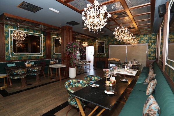 Un comedor con una mesa larga, sillas y un sofá. Hay candelabros y una planta en maceta.