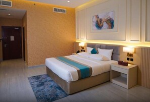 A hotel room with a large bed, bedside tables, a nightstand, a wall-mounted artwork, and a door in the background. - Concorde Creek View Hotel (Dubai)