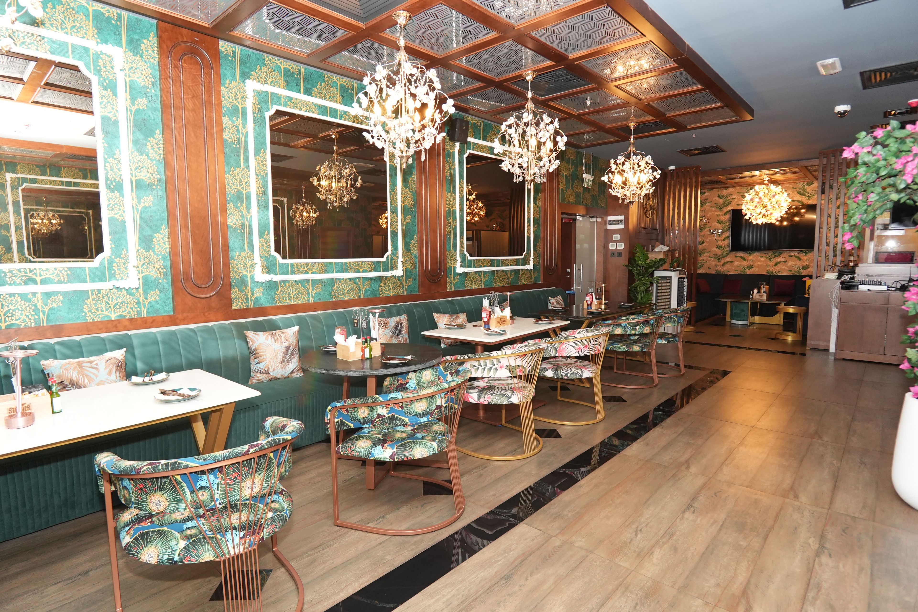 A restaurant with a green upholstered booth seating area, patterned chairs, and chandeliers.