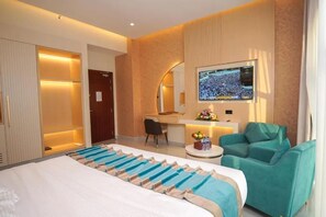 Una habitación de hotel con una cama, un escritorio, un televisor y dos sillones color turquesa.