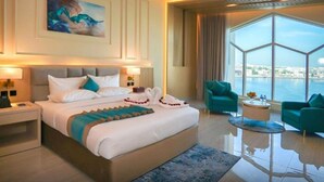 A modern hotel room with a large bed, two armchairs, a round coffee table, and a view of the city through large windows. - Concorde Creek View Hotel (Dubai)