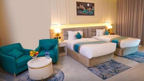 A hotel room with two beds, a teal armchair, a round coffee table with fruit, and a painting on the wall. - Concorde Creek View Hotel (Dubai)