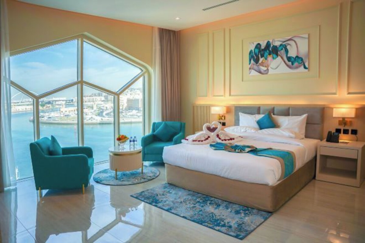 A modern hotel room with a large window offering a city view, a bed with decorative pillows, and a round side table.
