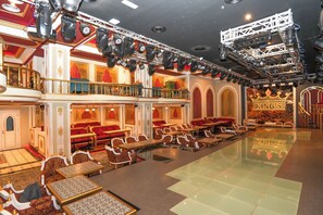 Un vestíbulo de hotel espacioso y elegantemente decorado, con varias zonas de estar, un escenario con equipo de iluminación y un cartel llamativo que dice 'King's'.