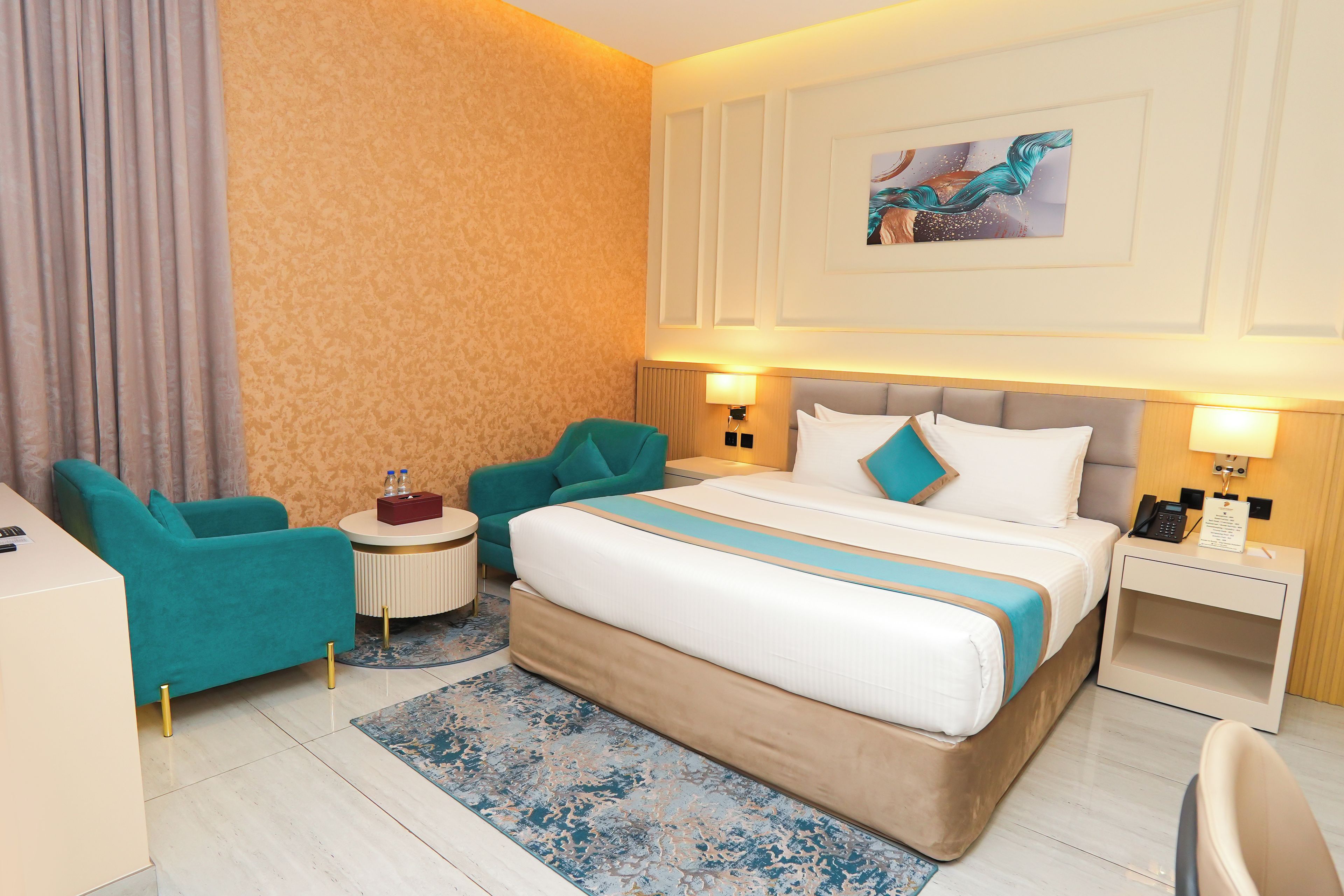 A hotel room with a large bed, two armchairs, a small round table, and a nightstand with a phone and a lamp.