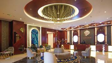 A hotel lobby with a reception desk, seating area, and a large chandelier.