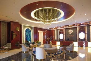 A hotel lobby with a reception desk, seating area, and a large chandelier.