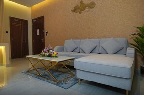 A modern living room with a light grey sofa, a white coffee table with a floral centerpiece, and a blue patterned rug. - Concorde Creek View Hotel (Dubai)