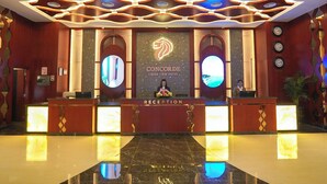 A hotel reception area with a marble floor, a reception desk, and a large logo on the wall. - Concorde Creek View Hotel (Dubai)
