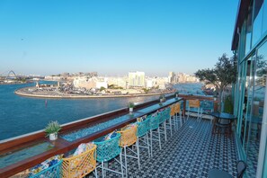 Un bar frente al agua con terraza, vistas de la ciudad y cielo despejado.