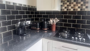 A kitchen with black and white tiles, a black countertop, a coffee maker, a toaster, and a gas stove. - 2 Bed Flat - Sleeps 4 - Parking - Wifi (London)
