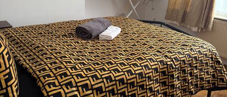 A neatly made bed with patterned bedding, a small table with a vase, and a picture on the wall.