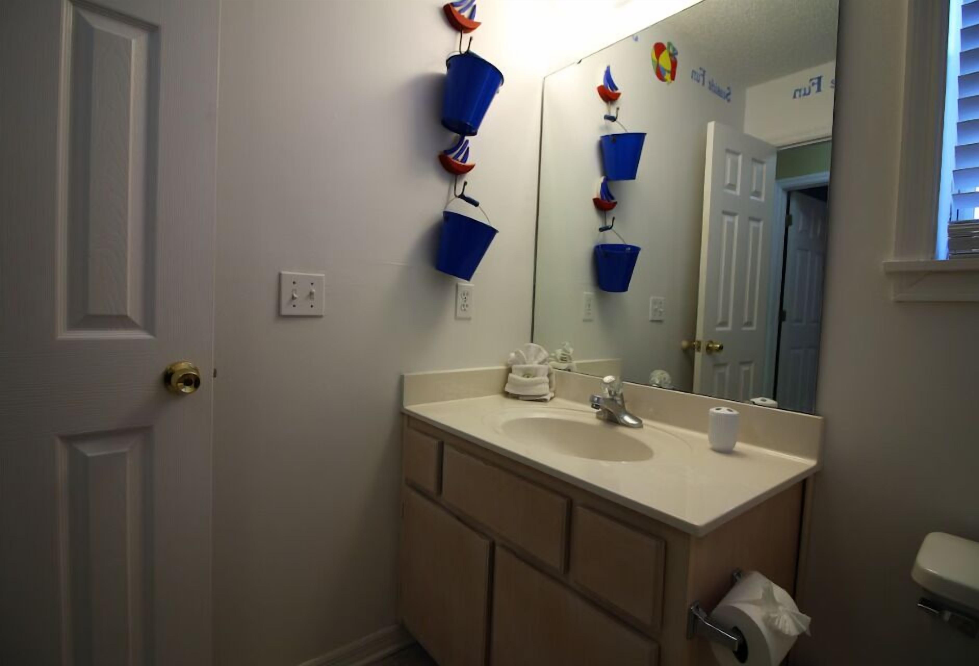 Un baño con lavamanos, espejo e inodoro. Hay elementos decorativos azules y rojos colgados en la pared.