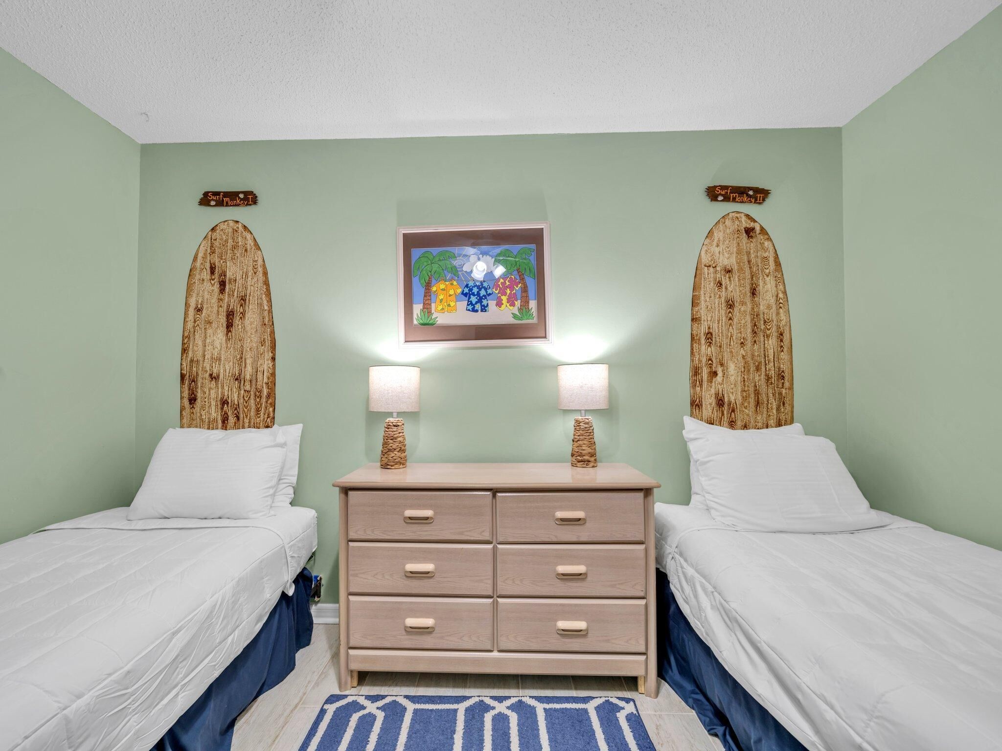A room with two beds, a dresser, and two surfboard-shaped wall decorations.