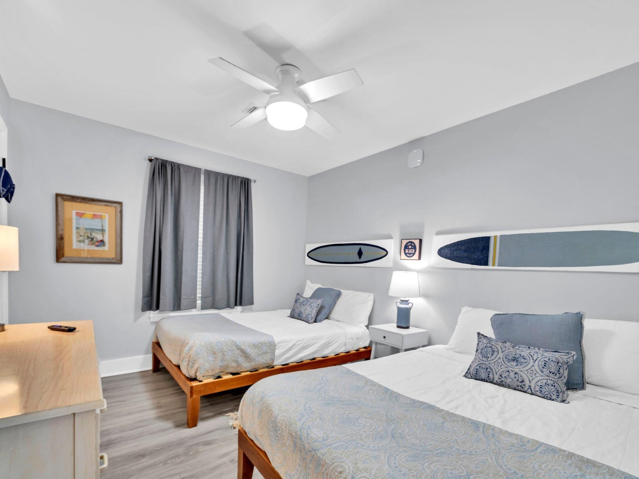 A modern hotel room with two beds, a ceiling fan, a desk, and a nightstand.