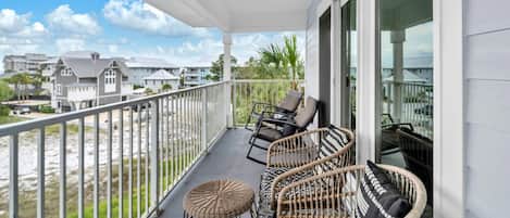 A balcony with wicker furniture and a view of the beach and other buildings.