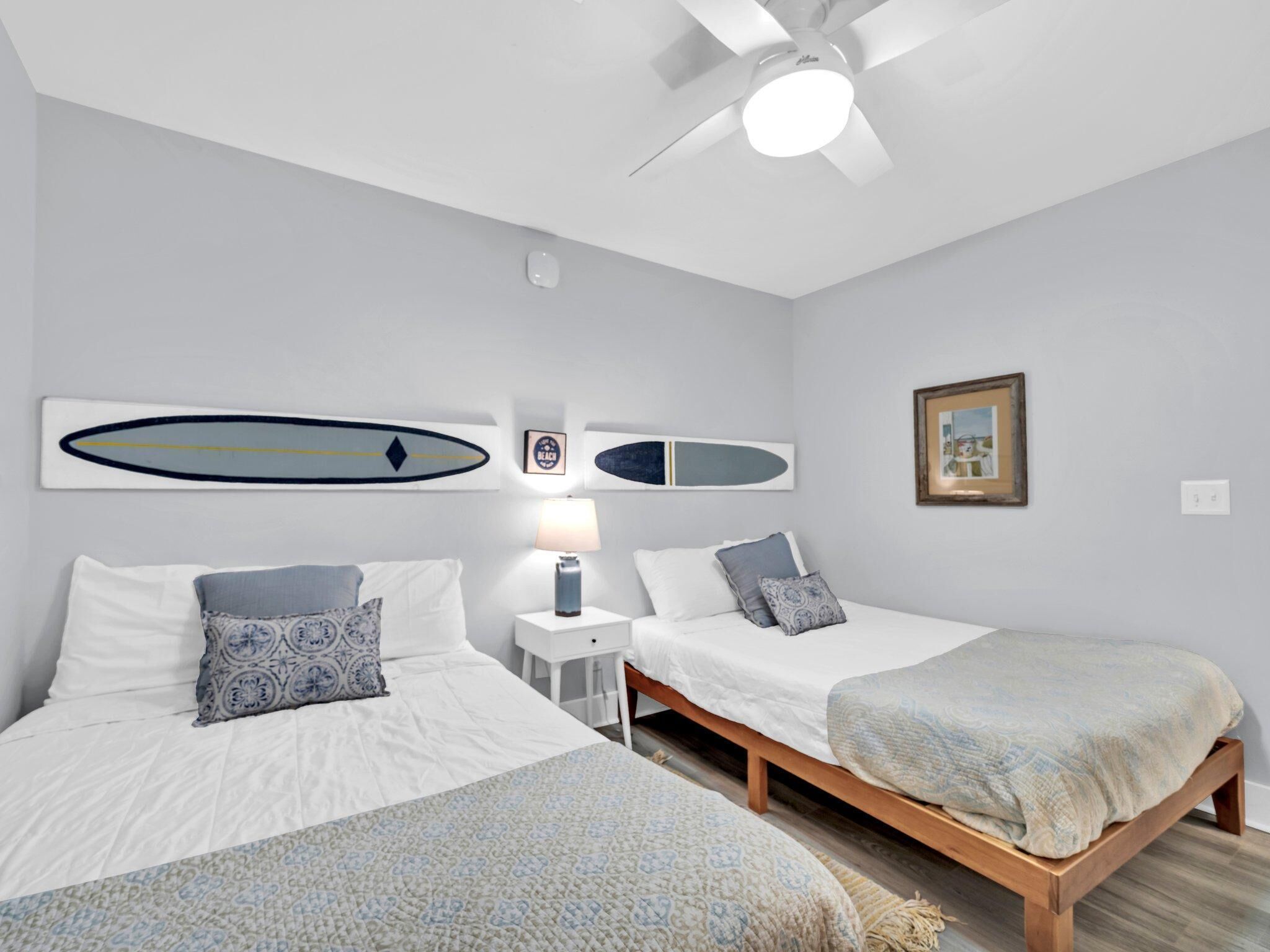 A bedroom with two beds, a ceiling fan, and surfboard-themed wall art.