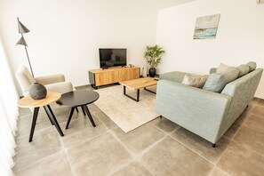 Un salon moderne avec un canapé, une table basse, un téléviseur et une plante.