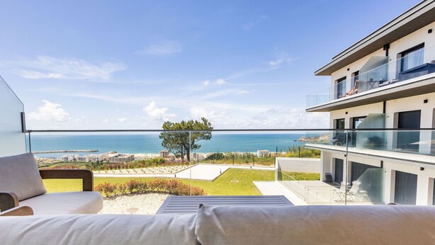 A balcony with a view of the sea, a grassy area, and a modern building.