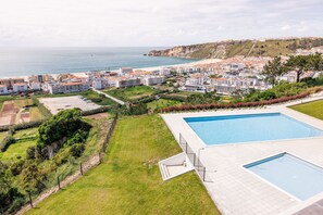 A residential area with a large swimming pool, a beach, and a hilly landscape in the background.