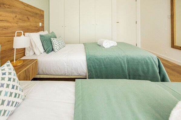 A hotel room with two beds, a wooden headboard, a nightstand with a lamp, and a mirror on the wall.