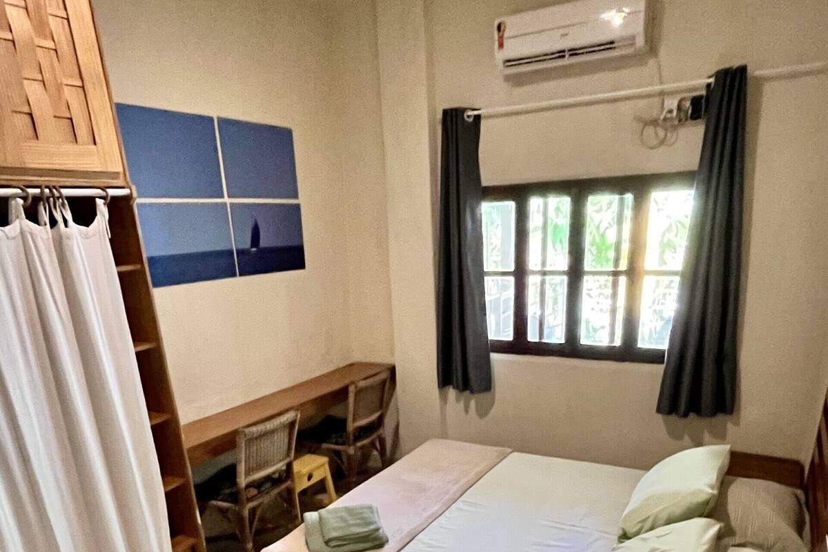 Un dormitorio con cama, escritorio, silla, armario y ventana con cortinas.