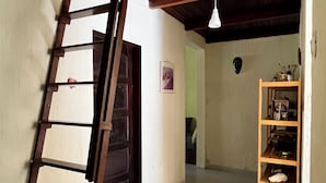 Ein schmaler Flur mit einer Holzleiter, die an einer Wand lehnt, einem gefliesten Boden und einem Holzbodenregal mit verschiedenen Gegenständen.