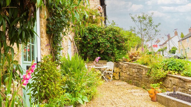 Ein Garten mit einer Steinmauer, einem Holzstuhl und einem Tisch.