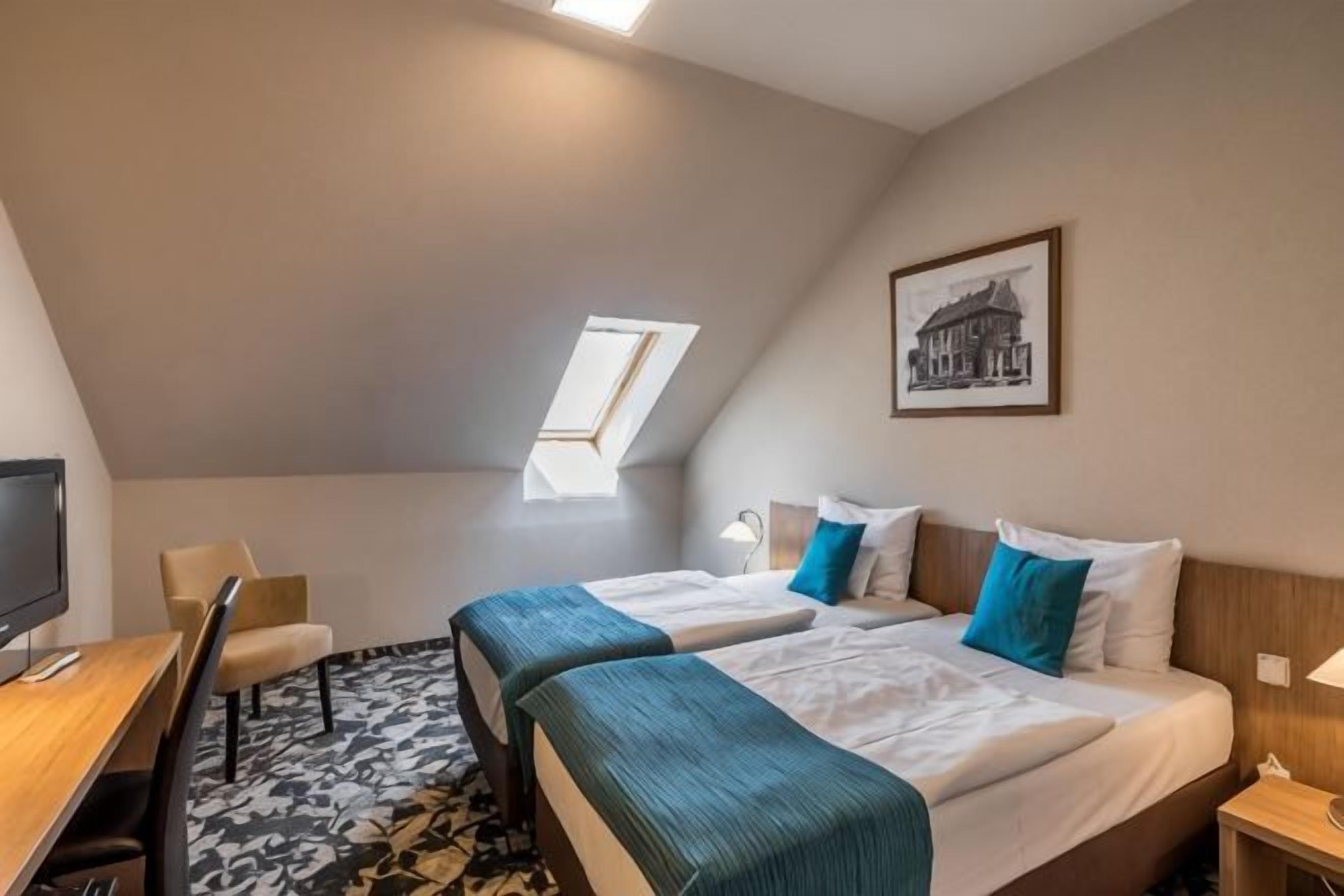 A hotel room with two beds, a desk, a chair, a TV, and a window.